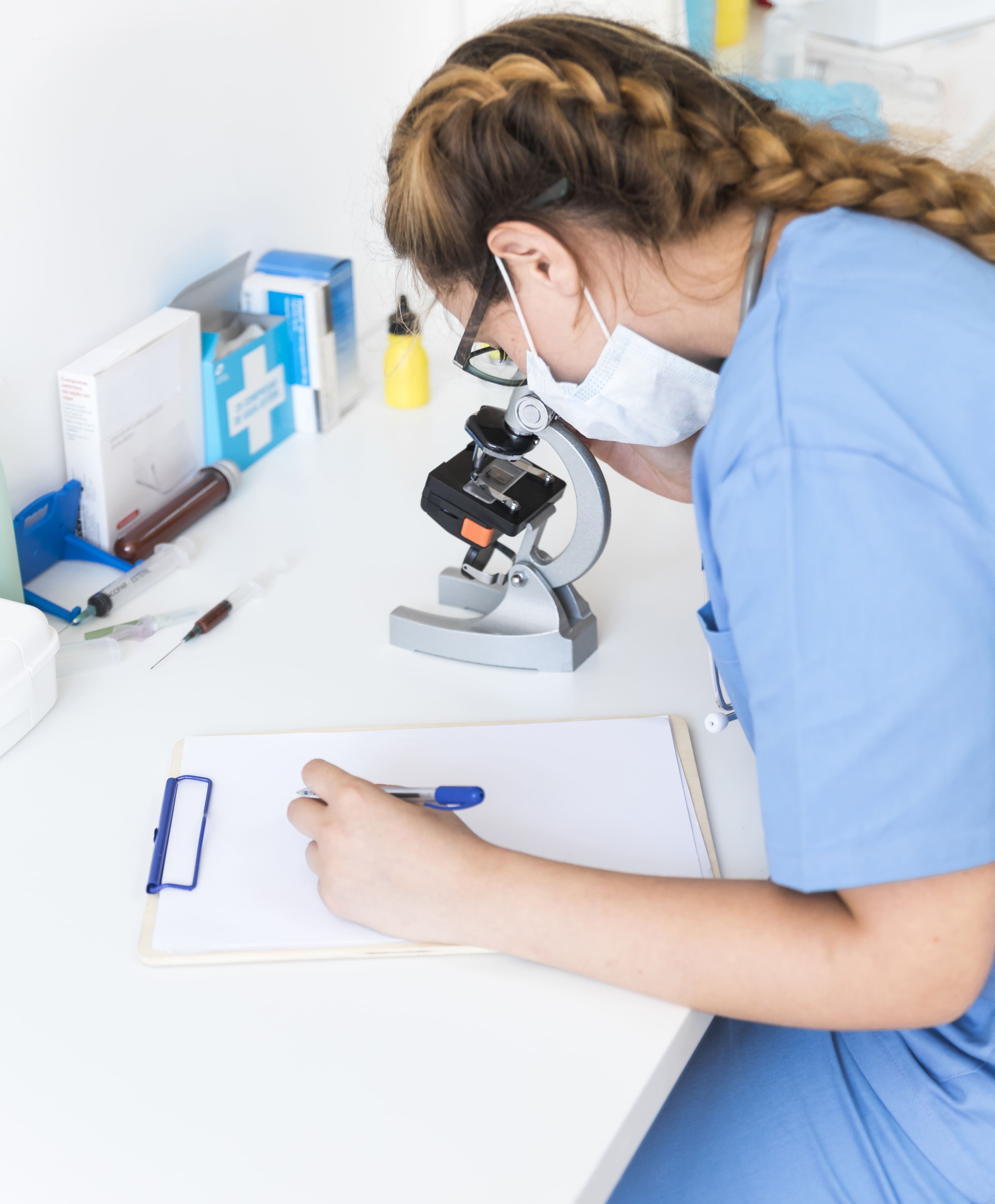 female-doctor-looking-through-microscope-writing-clipboard-laboratory (1)-1